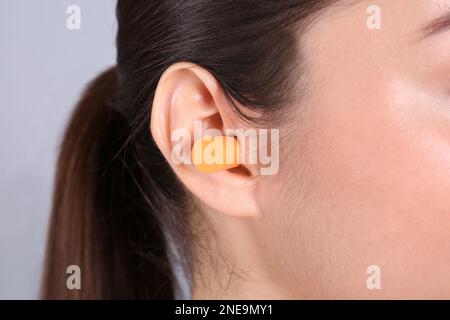 Jeune femme portant un bouchon d'oreille en mousse sur fond gris, gros plan Banque D'Images