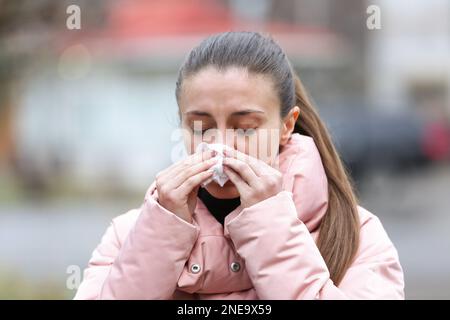 Femme malade avec des mouchoirs en papier éternuant à l'extérieur Banque D'Images