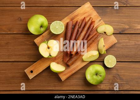 Délicieux rouleaux de cuir de fruits, pommes et limes sur table en bois, plat Banque D'Images