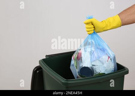 Homme jetant un sac poubelle dans la poubelle sur fond clair, gros plan. Espace pour le texte Banque D'Images