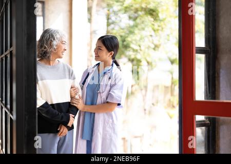 Jeune aidant une femme âgée à marcher. Infirmière aidant sa vieille patiente à la maison de soins. Femme âgée avec bâton de marche aidé par Banque D'Images