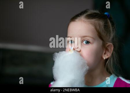 Portrait d'une petite fille étonnante avec des cheveux justes tenant manger délicieux coton blanc bonbon candyfloss regardant l'appareil-photo. Banque D'Images