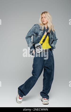 femme blonde avec ensemble en denim bleu et baskets tendance sur fond gris Banque D'Images