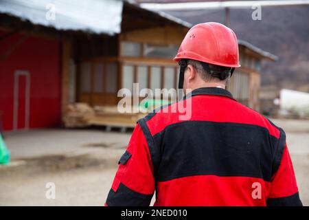 Un gros plan d'un homme dans une veste rouge et noire portant un casque de sécurité. Banque D'Images