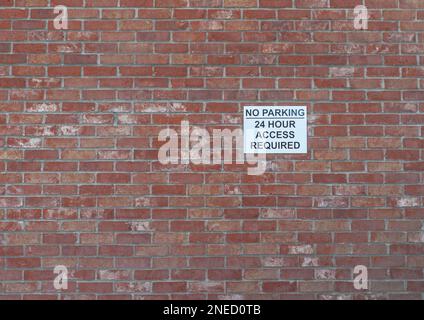 27 janvier 2022 - Un panneau d'avertissement noir et blanc pour l'absence de parking et l'accès 24 heures sur 24 attaché à un mur de briques rouges. Banque D'Images