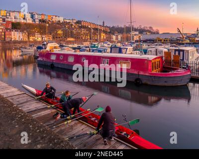 Les rameurs préparent leur bateau au lever du soleil à Bristol Marina, avec les maisons en terrasse colorées de Cliftonwood au loin. Bristol. ROYAUME-UNI. Banque D'Images