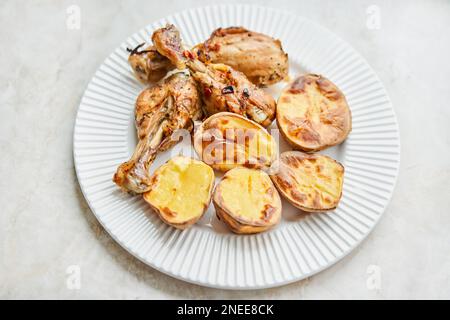 Poulet cuit en morceaux avec des pommes de terre et des oignons sur un plat blanc. Cuisine maison. Aliments sains, cuits sans huile ni sel. Banque D'Images