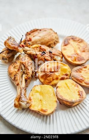 Poulet cuit en morceaux avec des pommes de terre et des oignons sur un plat blanc. Cuisine maison. Aliments sains, cuits sans huile ni sel. Banque D'Images