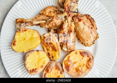 Poulet cuit en morceaux avec des pommes de terre et des oignons sur un plat blanc. Cuisine maison. Aliments sains, cuits sans huile ni sel. Banque D'Images