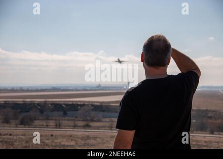 Un adulte légèrement chauve habillé de noir regardant et pointant pendant que les avions décollage de la piste de l'aéroport Banque D'Images