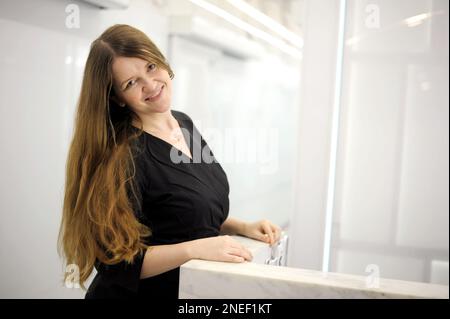 belle femme dans une salle blanche de bureau en robe noire avec de longs cheveux coulant a jeté sa tête et regarde dans l'espace cadre pour le texte sourire pas de fréquence de maquillage Banque D'Images