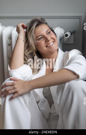 Élégante femme d'affaires en costume blanc se repose contre le mur et regarde loin . Décorateur d'intérieur. Émotions positives. Banque D'Images