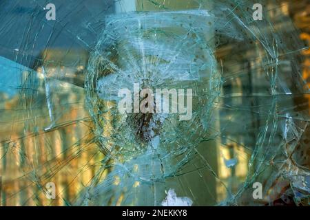 Un trou dans la vitre avec une balle pendant une fusillade militaire. Les fissures se propagent autour du trou. Cadre de fenêtre sale. Vue sur la rue depuis l' Banque D'Images