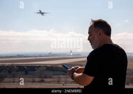 Un adulte légèrement chauve habillé de noir regardant et pointant pendant que les avions décollage de la piste de l'aéroport Banque D'Images