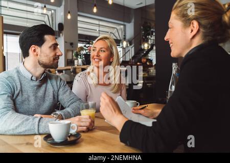 Un organisateur de mariage rencontre ses clients, un jeune couple dans un café pour leur première réunion Banque D'Images