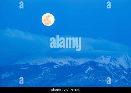 Pleine lune s'élevant au-dessus des montagnes enneigées de la Sal au crépuscule en hiver près de Moab, Utah. Banque D'Images