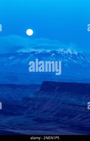 Pleine lune s'élevant au-dessus des montagnes enneigées de la Sal au crépuscule en hiver près de Moab, Utah. Banque D'Images