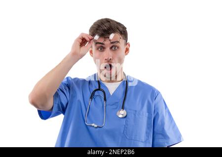 Médecin en uniforme et avec un stéthoscope montre des émotions de surprise et d'horreur en ouvrant sa bouche et en levant ses lunettes. Banque D'Images