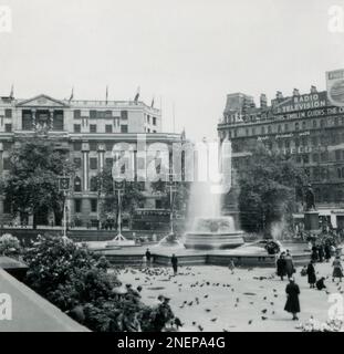 Londres, Angleterre. 1953. Une vue de Trafalgar Square qui a été décoré de bannières, en particulier pour le couronnement de la reine Elizabeth II, qui a eu lieu le 2nd juin 1953. Visibles au loin sont South Africa House et le Grand Hôtel, le premier décoré pour le couronnement et le dernier avec des pancartes publicitaires. Banque D'Images