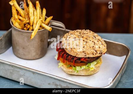 Hamburger végétarien à base de haricots, de légumes, de petits pains au ketchup et de pommes de terre frites dans une tasse vintage sur un plateau métallique. Portes vintage en arrière-plan. Banque D'Images