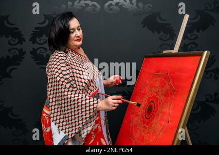 l'artiste dessine un mandala avec un pinceau et de la peinture rouge sur la toile Banque D'Images