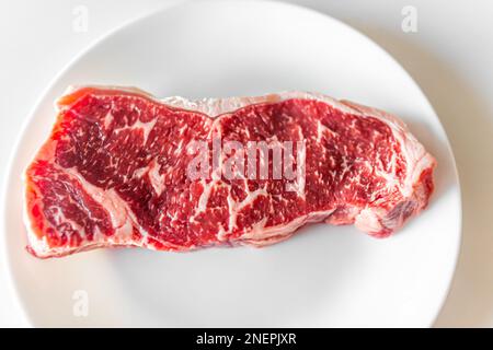 Vue du dessus plat de la bande rouge crue ou du steak de la ribeye coupé gros plan du boucher de texture coupé sur l'assiette blanche et le fond Banque D'Images