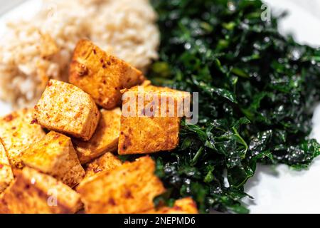 Cubes de tofu au curry faits maison, salade de kale massée et macro-gros plan de riz brun sur plaque blanche avec détail de texture des aliments Banque D'Images