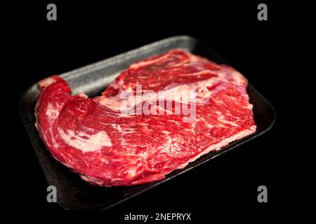 Steak de bœuf cru noir angus à trois pointes emballé avec fond noir comme photo en studio avec marbrure grasse et plateau Banque D'Images