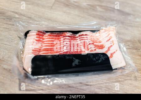 Stockage de bacon fumé non fumé acheté dans un emballage scellé sous vide en plastique avec des bandes grasses rouges et blanches de viande Banque D'Images