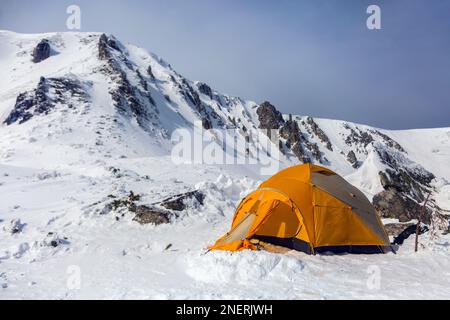 Les randonneurs ont installé une tente orange dans les montagnes d'hiver au milieu des rochers. Le sport alpinisme comme concept. Banque D'Images