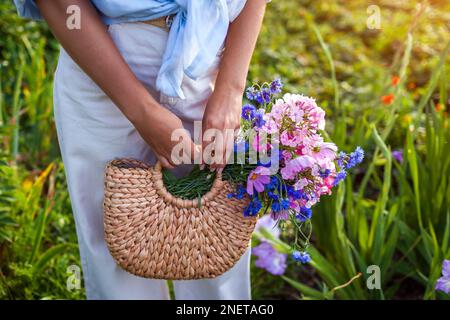 Gros plan sur un sac à main en paille plein de fleurs. Femme tenant un sac à main d'été avec un bouquet frais. Style boho rustique. Mode féminine Banque D'Images