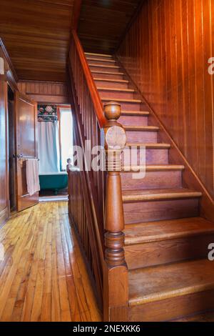 Escalier en bois menant au grenier et porte ouverte de la salle de bains principale avec baignoire sur pied de griffe à l'étage avec pinède colombienne à l'intérieur de la vieille maison. Banque D'Images