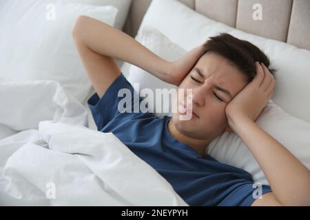 Un adolescent mignon souffrant de maux de tête en étant allongé au lit à la maison Banque D'Images