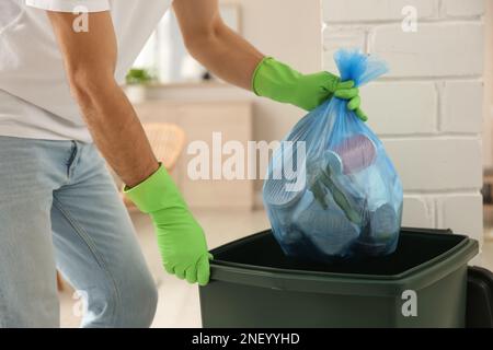 Homme jetant le sac poubelle dans la poubelle à la maison, gros plan Banque D'Images