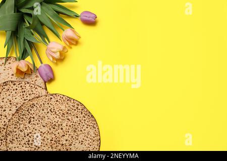 Savoureux matzos et fleurs fraîches sur fond jaune, plat avec espace pour le texte. Fête de la Pâque (Pesach) Banque D'Images
