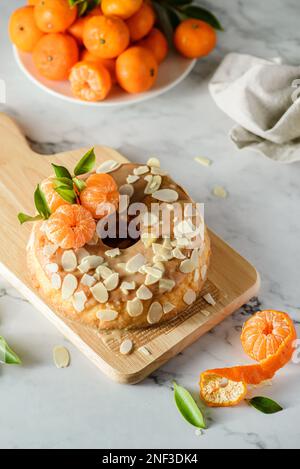 gâteau rond sans gluten à la farine d'amande avec mandarines sur fond de marbre blanc, orné de pétales d'amande Banque D'Images