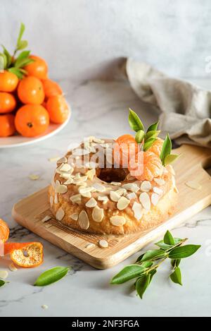 gâteau rond sans gluten à la farine d'amande avec mandarines sur fond de marbre blanc, orné de pétales d'amande Banque D'Images
