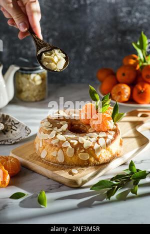 gâteau rond sans gluten à la farine d'amande avec mandarines sur fond de marbre blanc, orné de pétales d'amande Banque D'Images