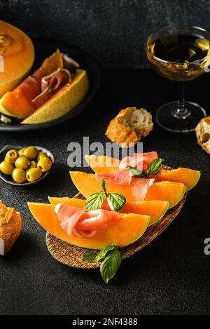 melon à parme, olives et baguette. en-cas pour le vin et un verre de vin à proximité, fond sombre Banque D'Images