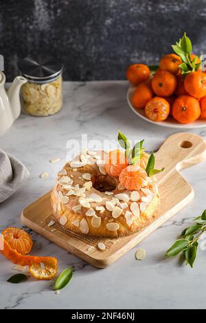 gâteau rond sans gluten à la farine d'amande avec mandarines sur fond de marbre blanc, orné de pétales d'amande Banque D'Images