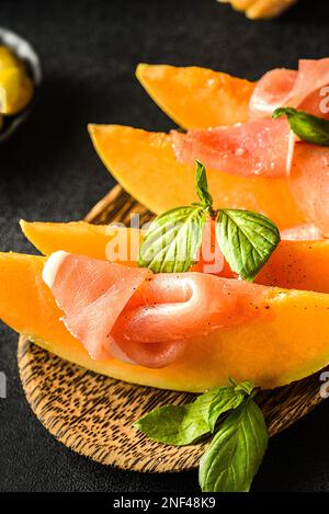 melon à parme, olives et baguette. en-cas pour le vin et un verre de vin à proximité, fond sombre Banque D'Images