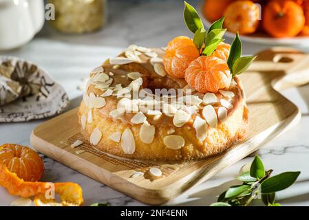 gâteau rond sans gluten à la farine d'amande avec mandarines sur fond de marbre blanc, orné de pétales d'amande Banque D'Images