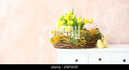 Couronne avec belles fleurs printanières et décor de Pâques sur la table près du mur de grunge dans la chambre Banque D'Images