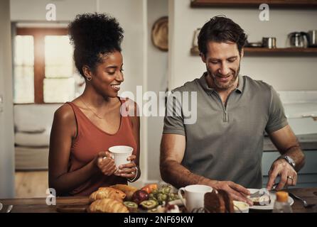 Je sais que vous aimez votre pain beurré... un jeune couple affectueux prenant le petit déjeuner dans leur cuisine à la maison. Banque D'Images