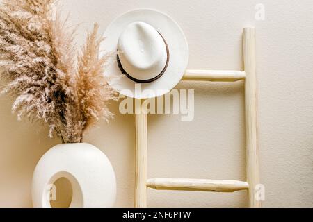 Échelle en bois sur le mur avec chapeau blanc dessus, pampas sec herbe dans le vase. Intérieur de style bohémien Banque D'Images