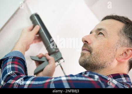 vue rapprochée de l'homme du caucase à l'aide d'un pistolet à silicone Banque D'Images