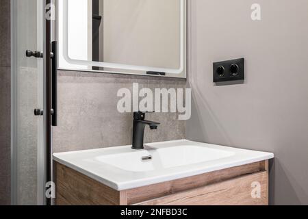 Gros plan d'un évier carré blanc en céramique sur un meuble-lavabo en bois. Raccords et robinet en métal ferreux. Sur le mur se trouve un miroir de créateur avec un blanc Banque D'Images