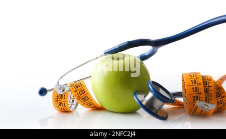 Pomme, stéthoscope et mètre à ruban se reflétant sur une table blanche et un fond blanc isolé représentant la santé, la nutrition et le contrôle du corps. Vue avant Banque D'Images