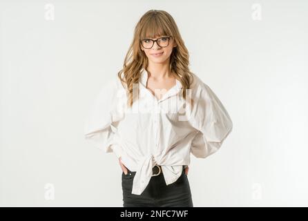 Une jeune femme portant des lunettes est debout avec confiance avec ses mains sur les hanches, regardant directement la caméra Banque D'Images