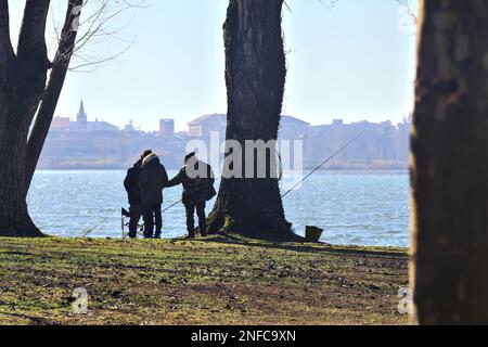 Pêcheur au bord du lac entre les arbres par une journée ensoleillée en hiver Banque D'Images